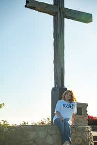 Person sitting on a stone wall with a cross in the background
