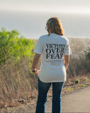 Person wearing a 'Victory Over Fear' t-shirt walking on a path with nature in the background