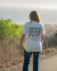Person wearing a 'Victory Over Fear' t-shirt walking on a path with nature in the background