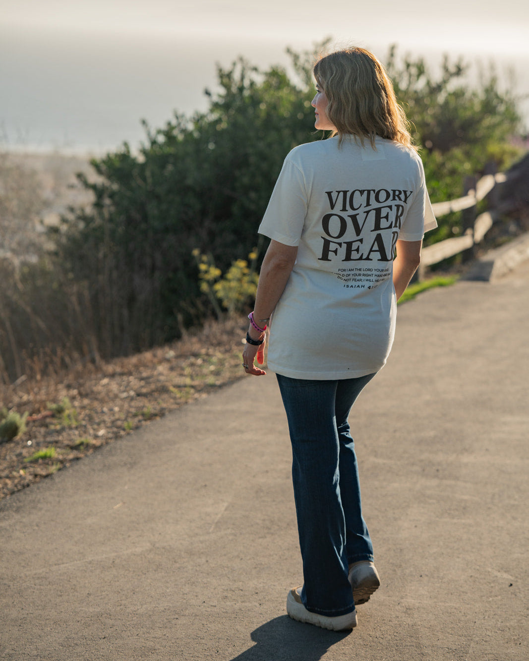 Person wearing a 'Victory Over Fear' t-shirt walking on a path with a scenic background.