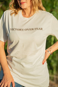 Person wearing a light gray t-shirt with 'Victory Over Fear' text, standing outdoors.