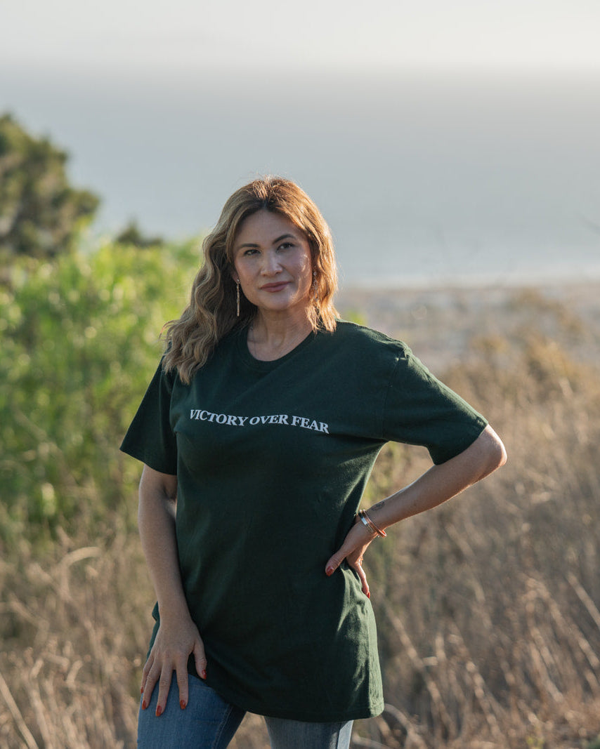 Woman wearing a green t-shirt with 'Victory Over Fear' text, standing outdoors.