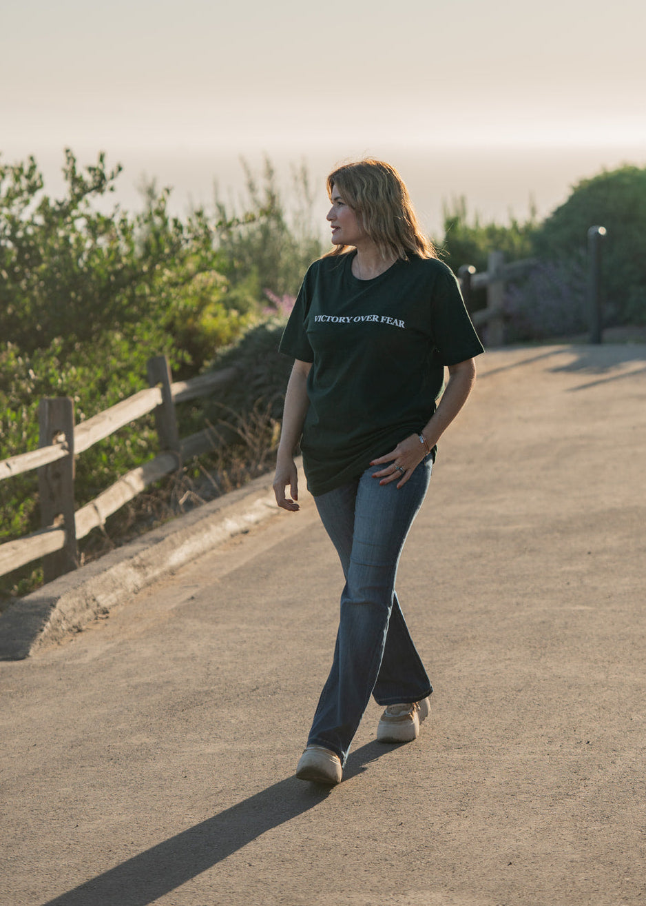 Person walking on a path with greenery and a wooden fence in the background