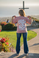 Person wearing a pink shirt with 'Child of God' text, standing in front of a cross.