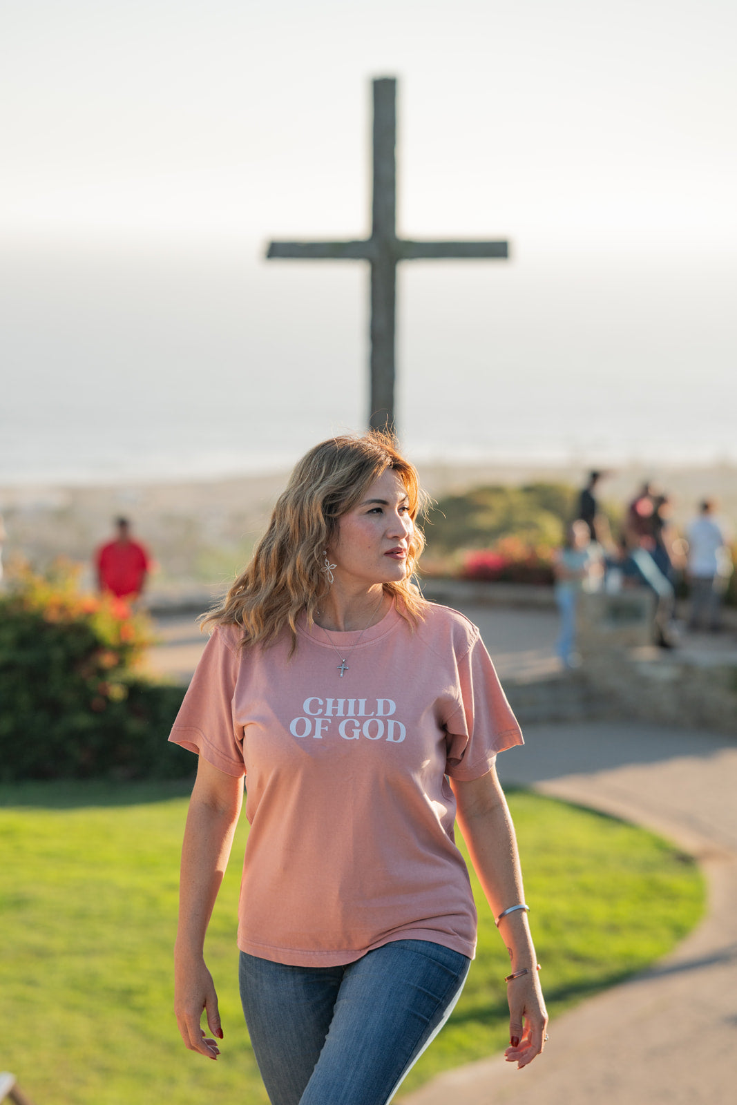 Woman wearing a 'Child of God' t-shirt walking outdoors with a cross in the background