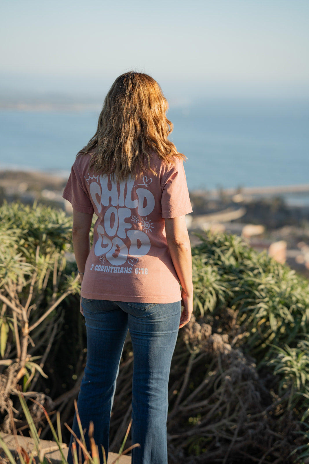 Person wearing a pink t-shirt with text, standing on a scenic overlook.