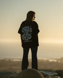 Person wearing a 'Child of God' shirt standing on a rocky outcrop with a sunset in the background
