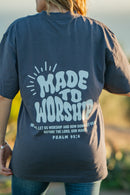 Person wearing a navy blue t-shirt with 'Made to Worship' text on the back, standing outdoors.