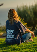Person sitting on grass wearing a t-shirt with text, surrounded by plants and sunset.
