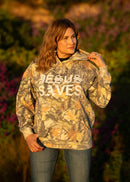 Person wearing a camouflage hoodie with 'Jesus Saves' text in an outdoor setting