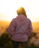 Person wearing a pink hoodie with 'God is Love' text, standing against a sunset background.